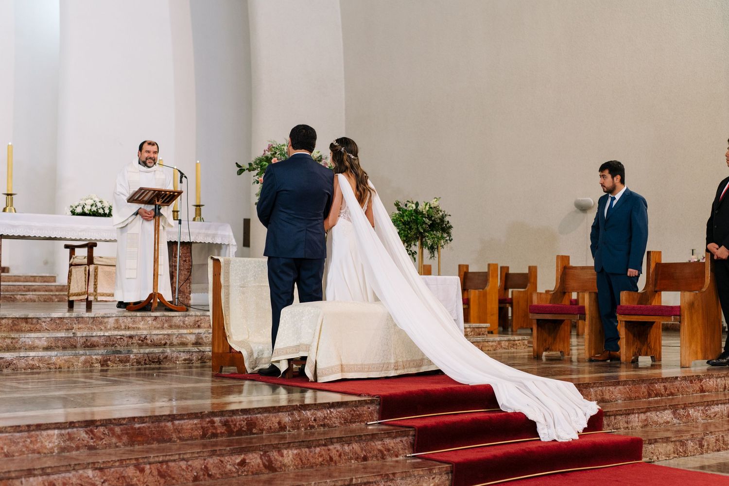 A wedding ceremony unfolds at the altar with the bride's train flowing down red-carpeted steps.