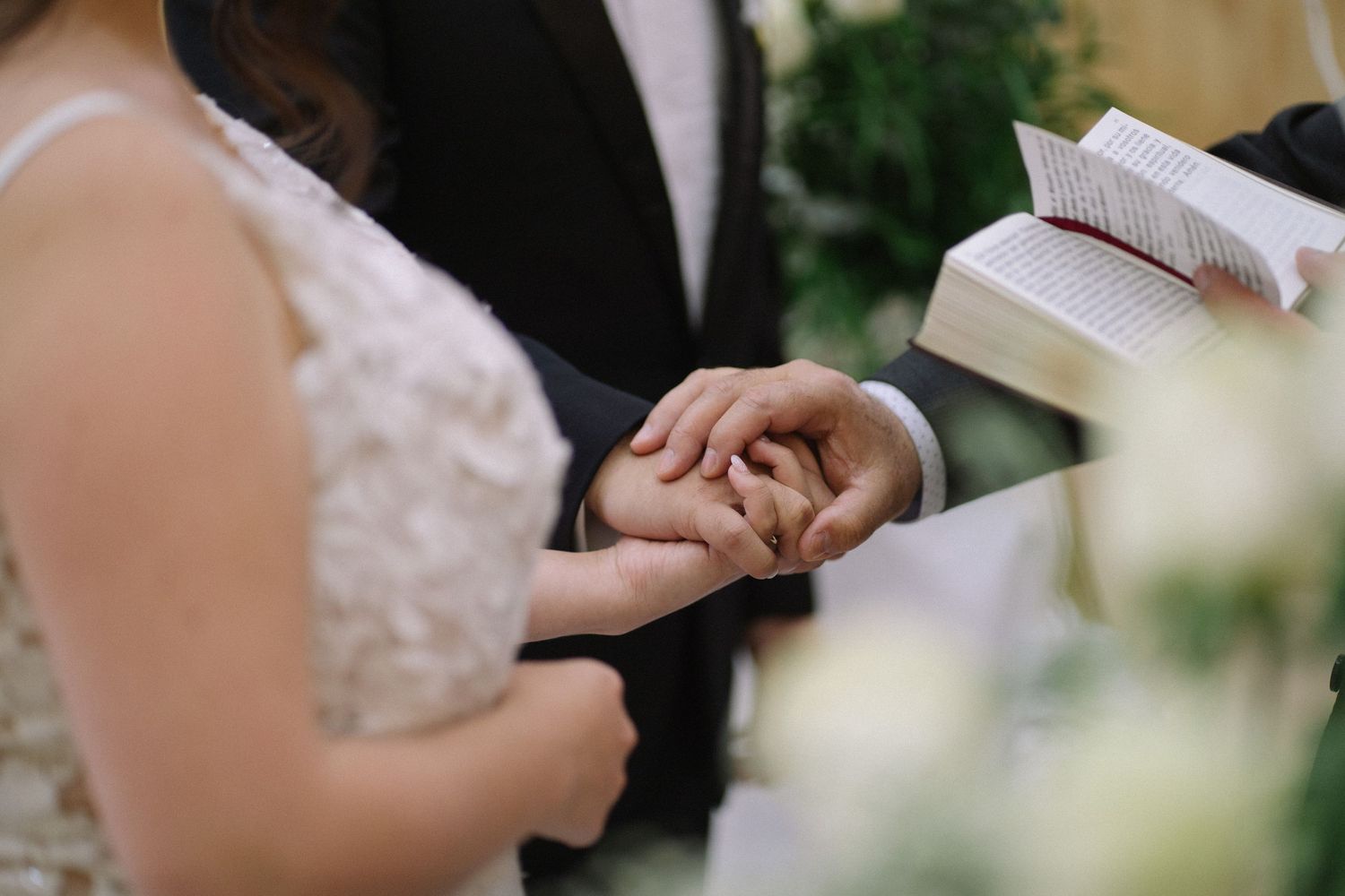 Close-up shot of hands exchanging rings during a wedding ceremony with white floral decorations.