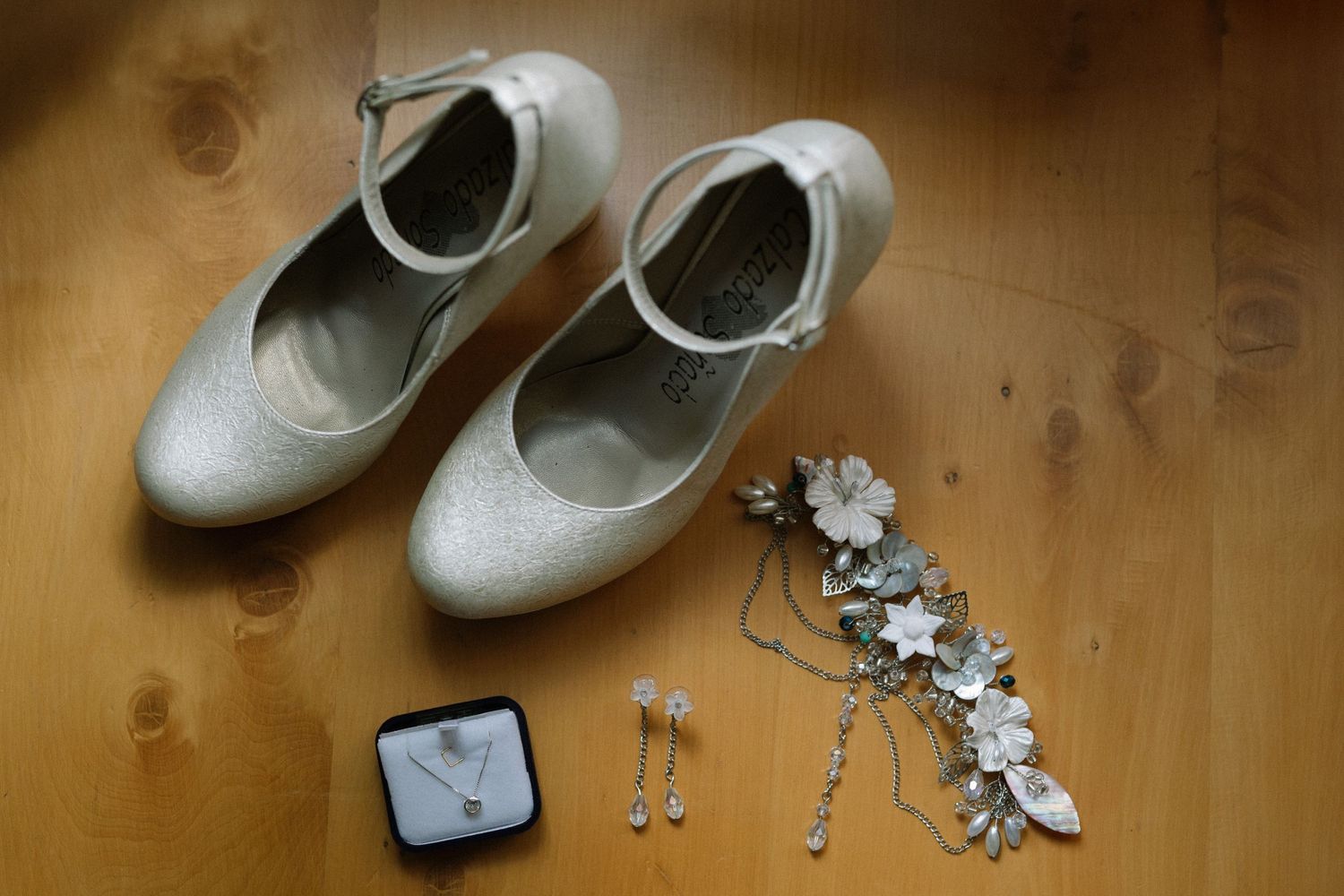 Bridal accessories including white shoes, jewelry and hair pieces on wooden surface.