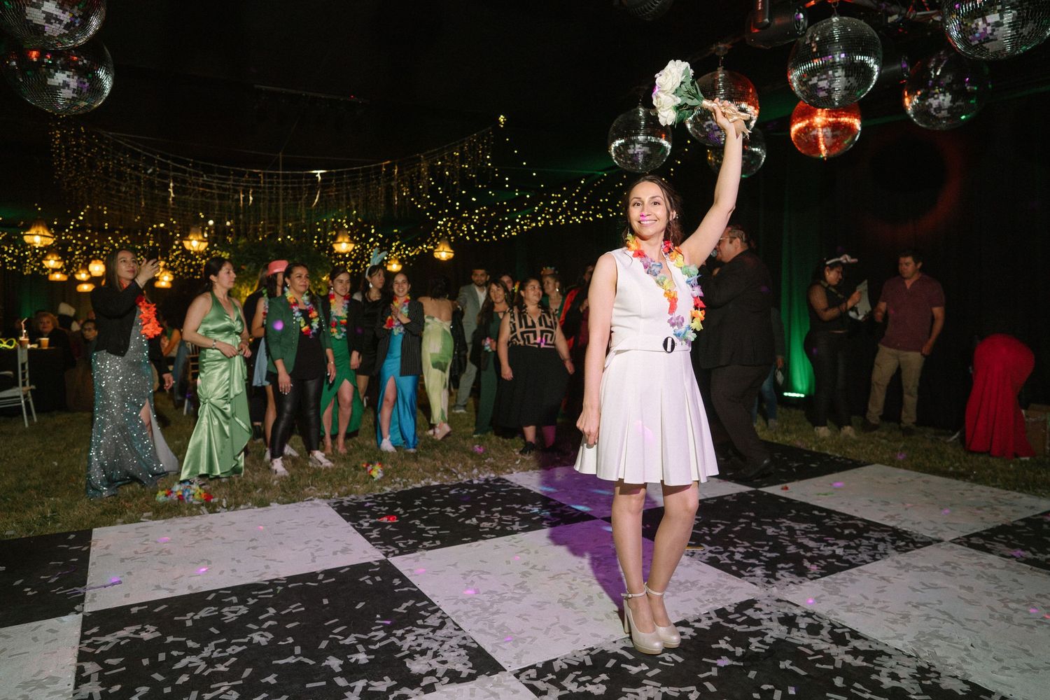 Someone in a pink dress celebrates on a checkered dance floor under string lights.