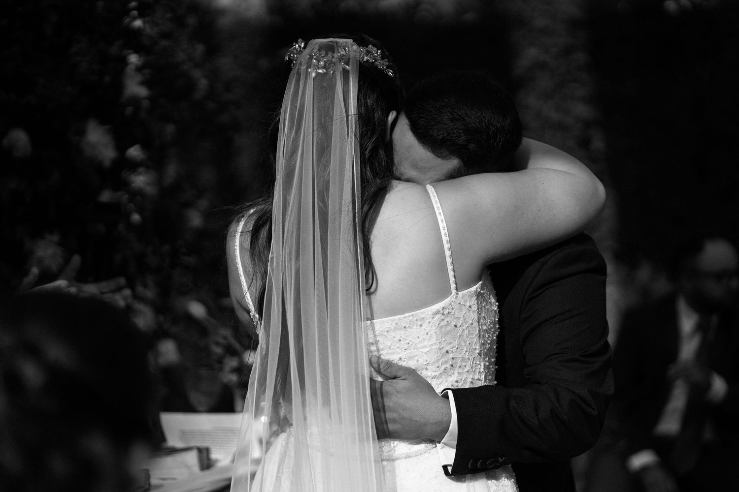Black and white photo of bride and groom sharing intimate embrace during outdoor wedding ceremony.