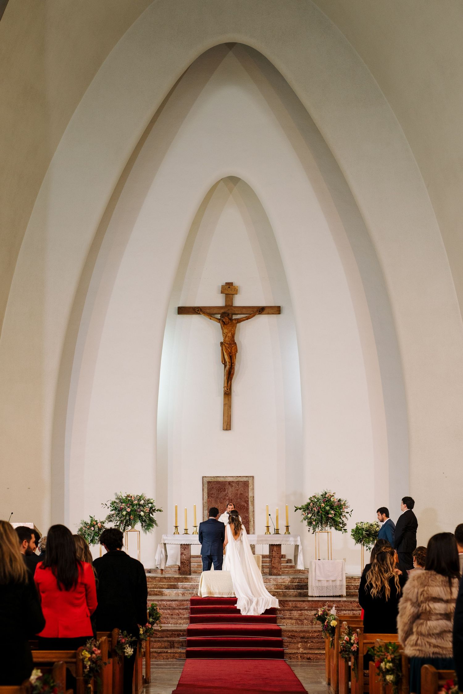 A church altar with soaring arched ceilings, crucifix, and wedding ceremony in progress.