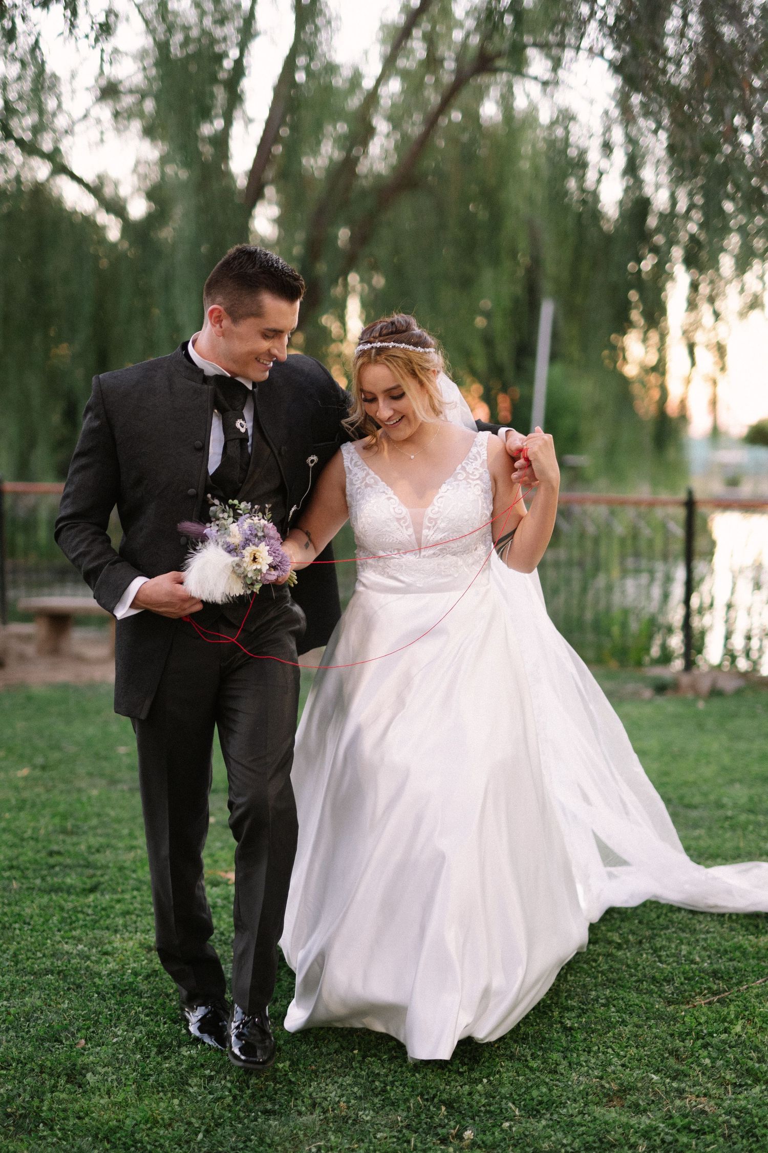 A newlywed couple walks together on grass, with the bride's white dress flowing in an outdoor garden setting.