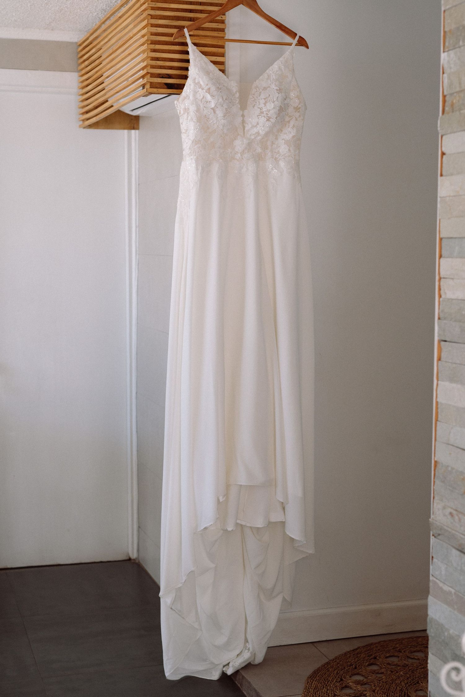 An elegant white wedding dress with lace details hanging on wooden hangers against a neutral wall.