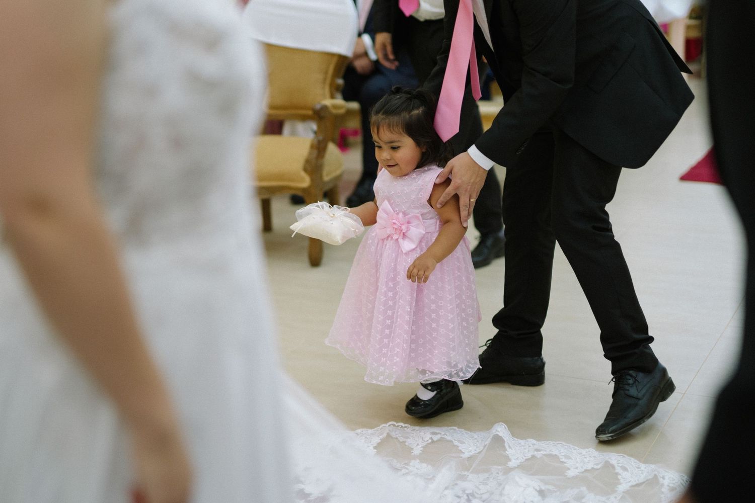 A small child in a pink dress stands among formal wedding attire during the ceremony.
