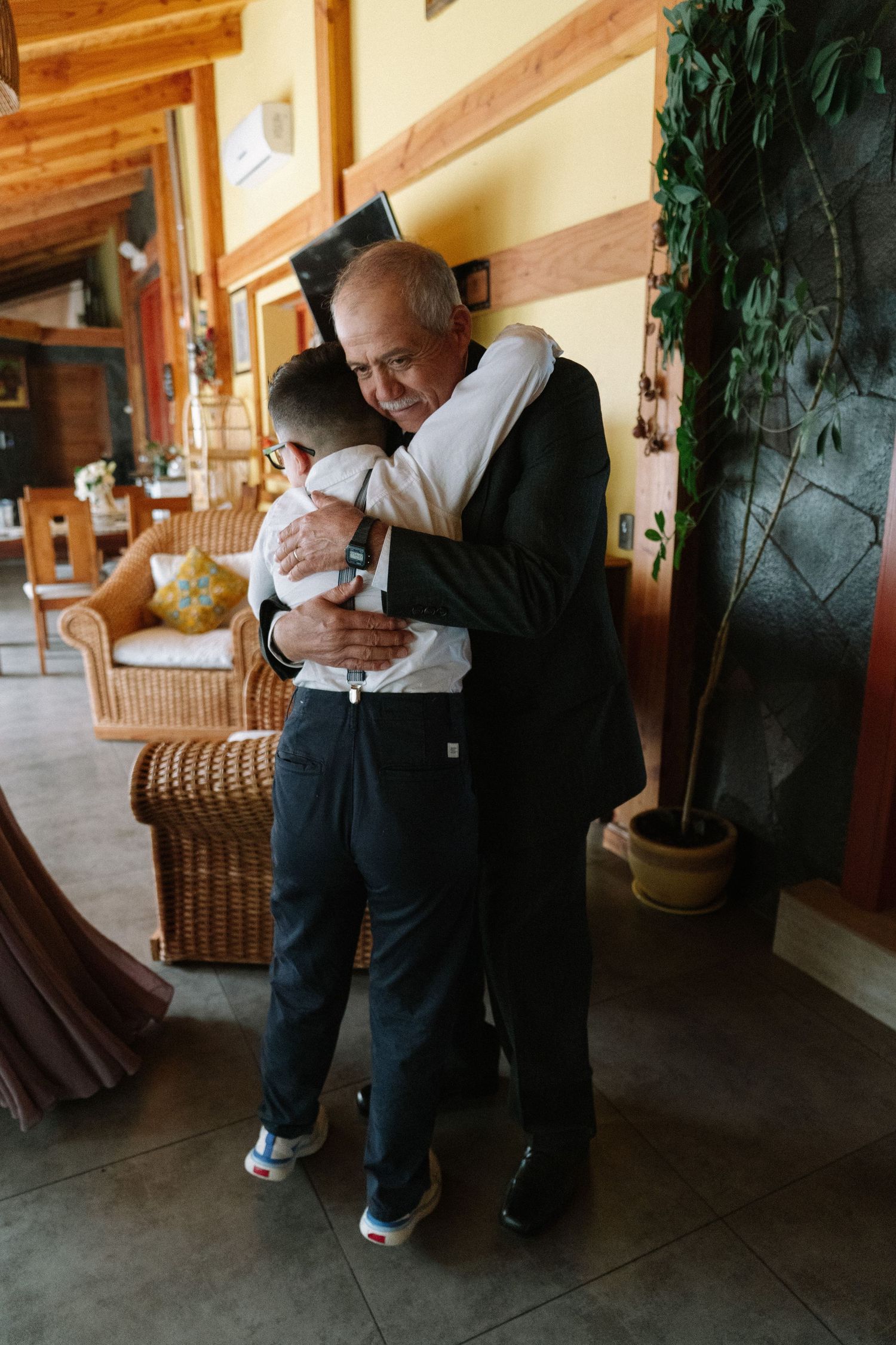 Elderly man sharing warm embrace with young boy in formal attire at indoor venue.