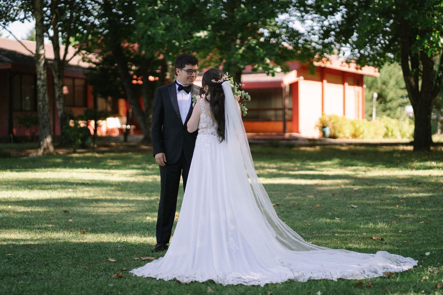 A wedding couple poses elegantly on a manicured lawn with a beautiful long train dress.