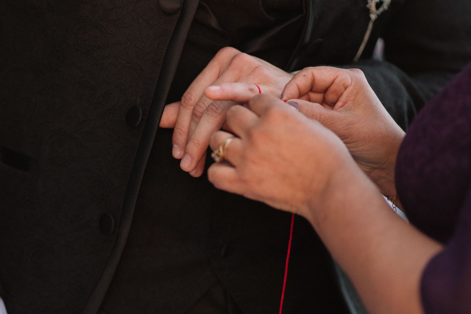 Close-up of hands exchanging rings during wedding ceremony with black formal attire visible.
