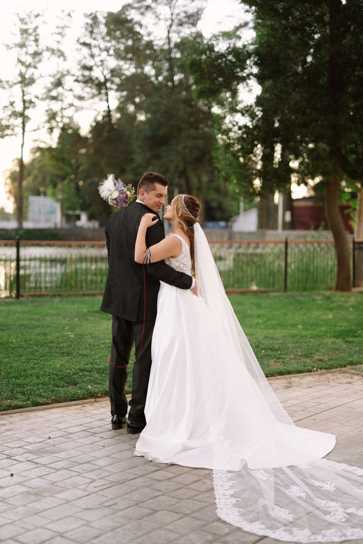 A romantic wedding moment captured in a park setting with a flowing white veil and formal attire.