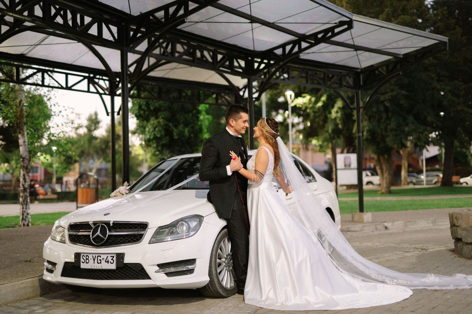 A romantic wedding portrait of a couple posing with their white Mercedes-Benz at dusk.