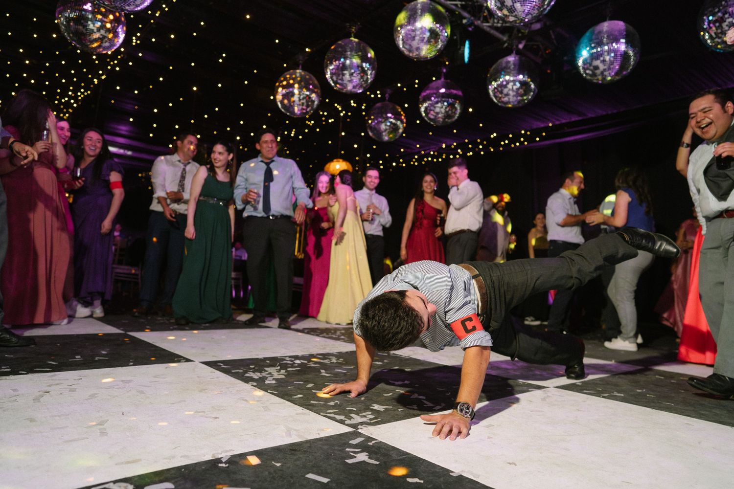 Party guests dance on a black and white checkered floor under sparkling disco balls.