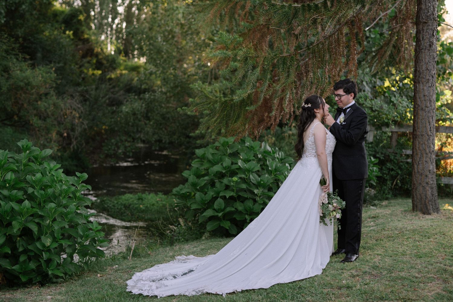 A romantic wedding moment captured in a lush garden setting with towering trees.