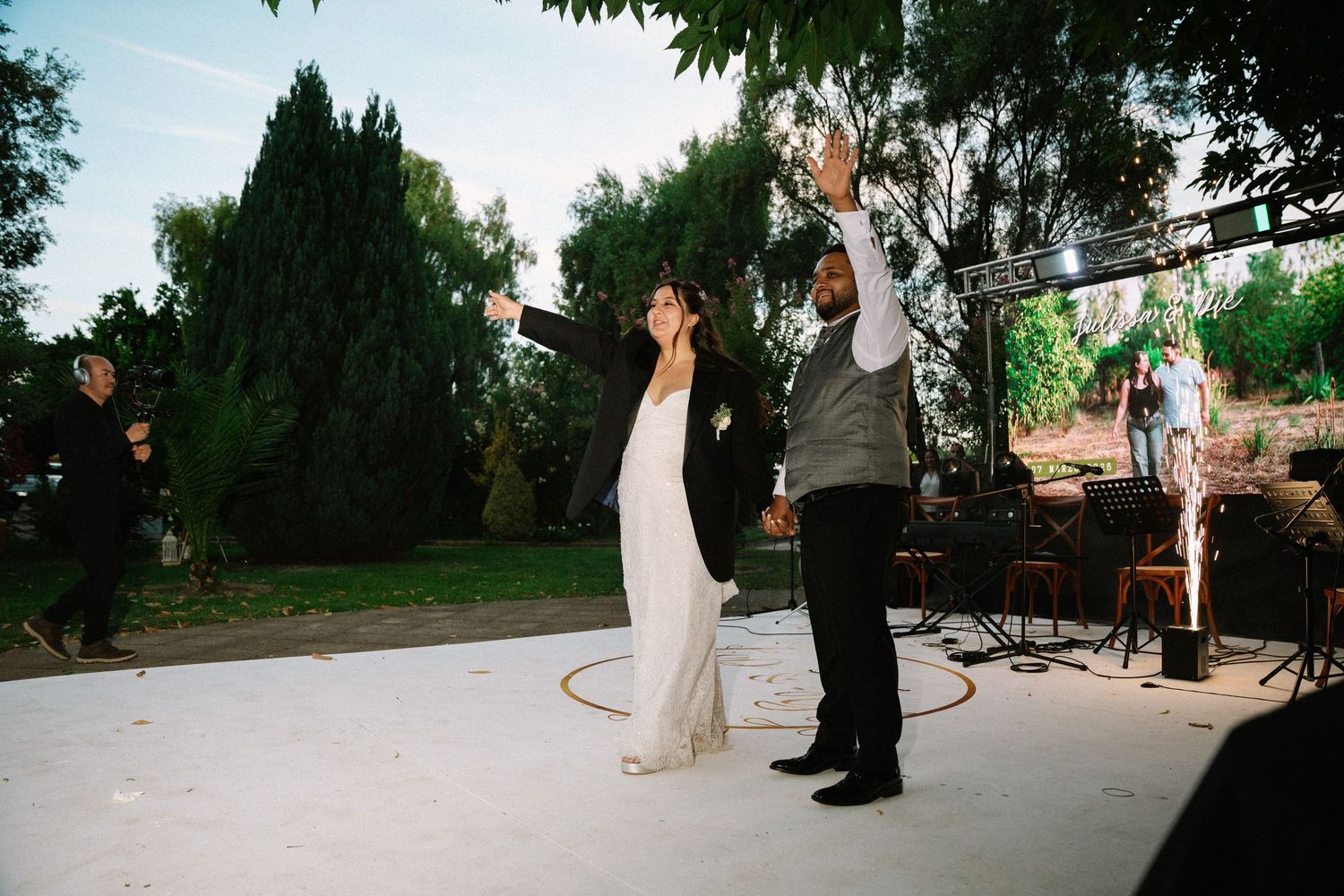 Bride and groom raise their hands joyfully during their first dance at an outdoor wedding reception.