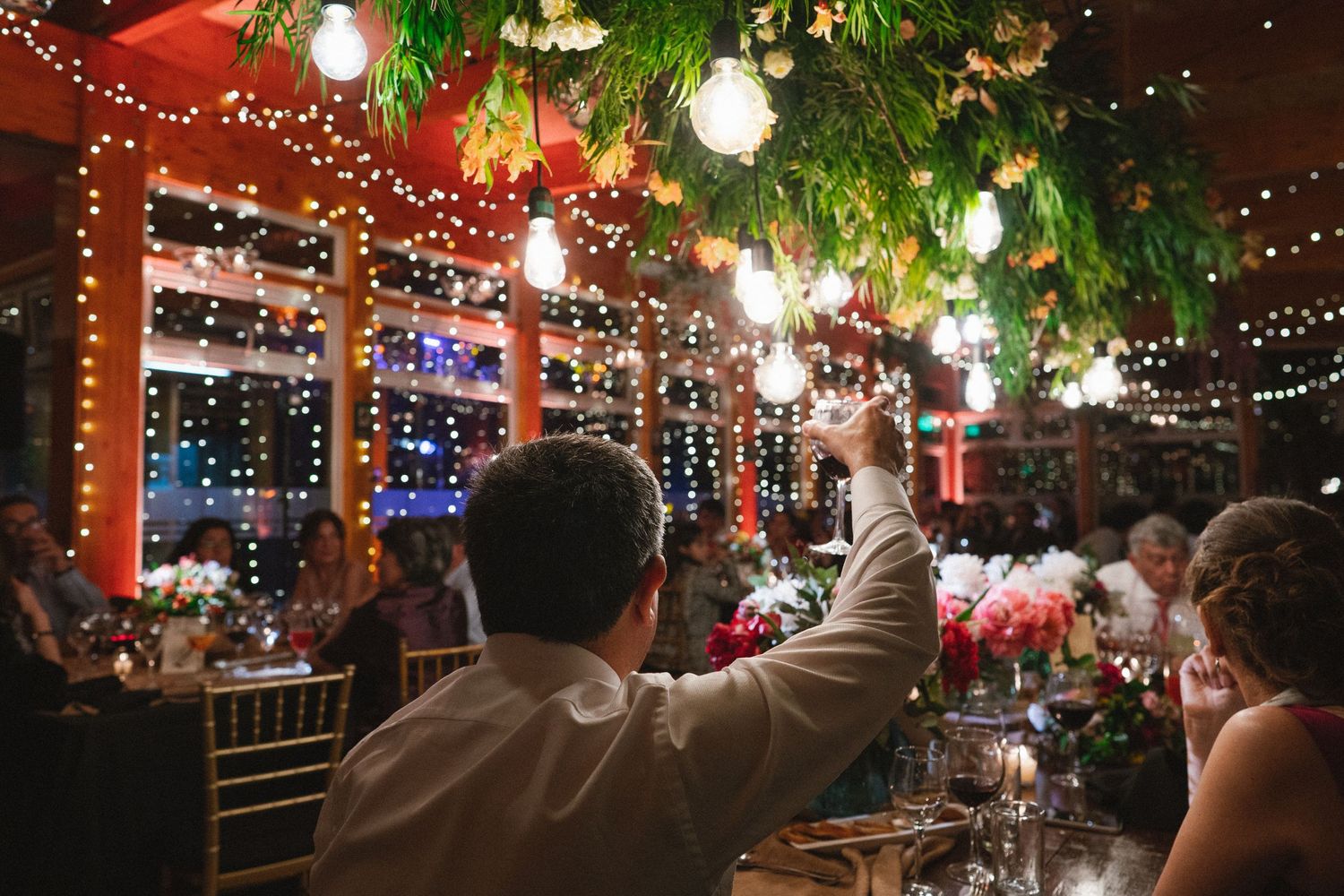 Wedding reception guests celebrating under string lights and greenery decorations.