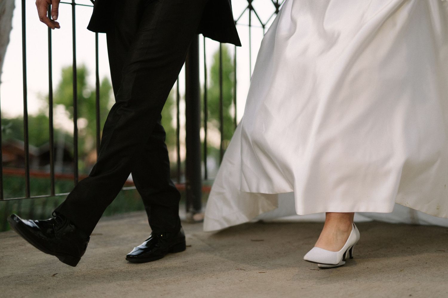 A close-up shot of formal wedding shoes, showing a black dress shoe and white bridal heel on a walkway.