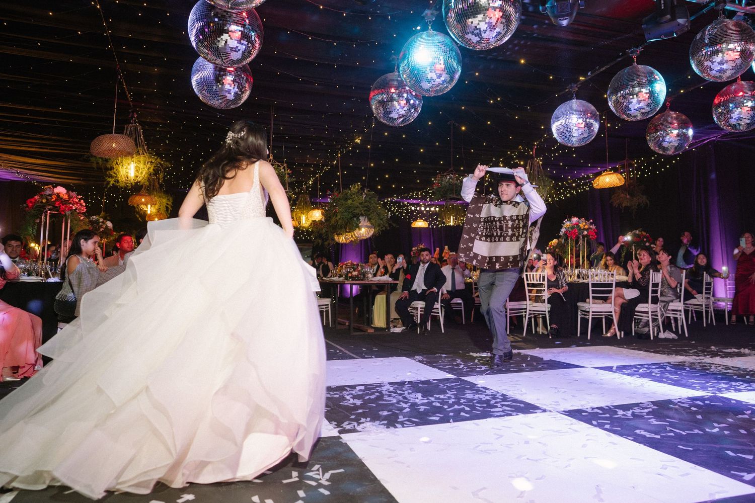 An elegant wedding reception venue with disco balls hanging from the ceiling and decorated tables.
