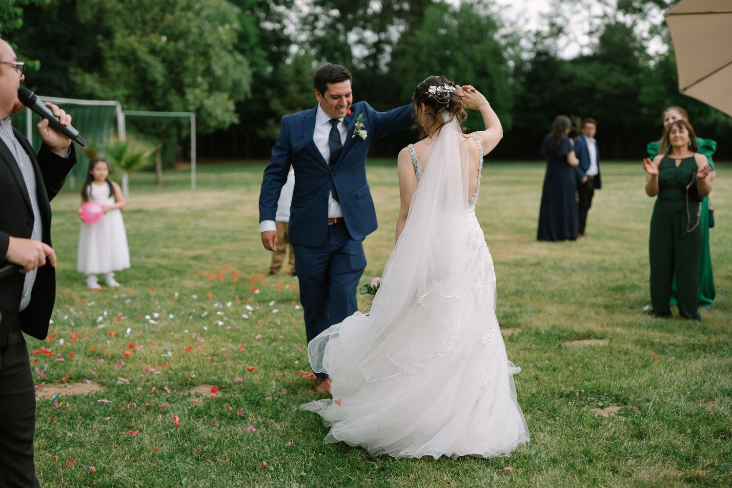 Newlyweds dancing on grass while wedding guests look on.