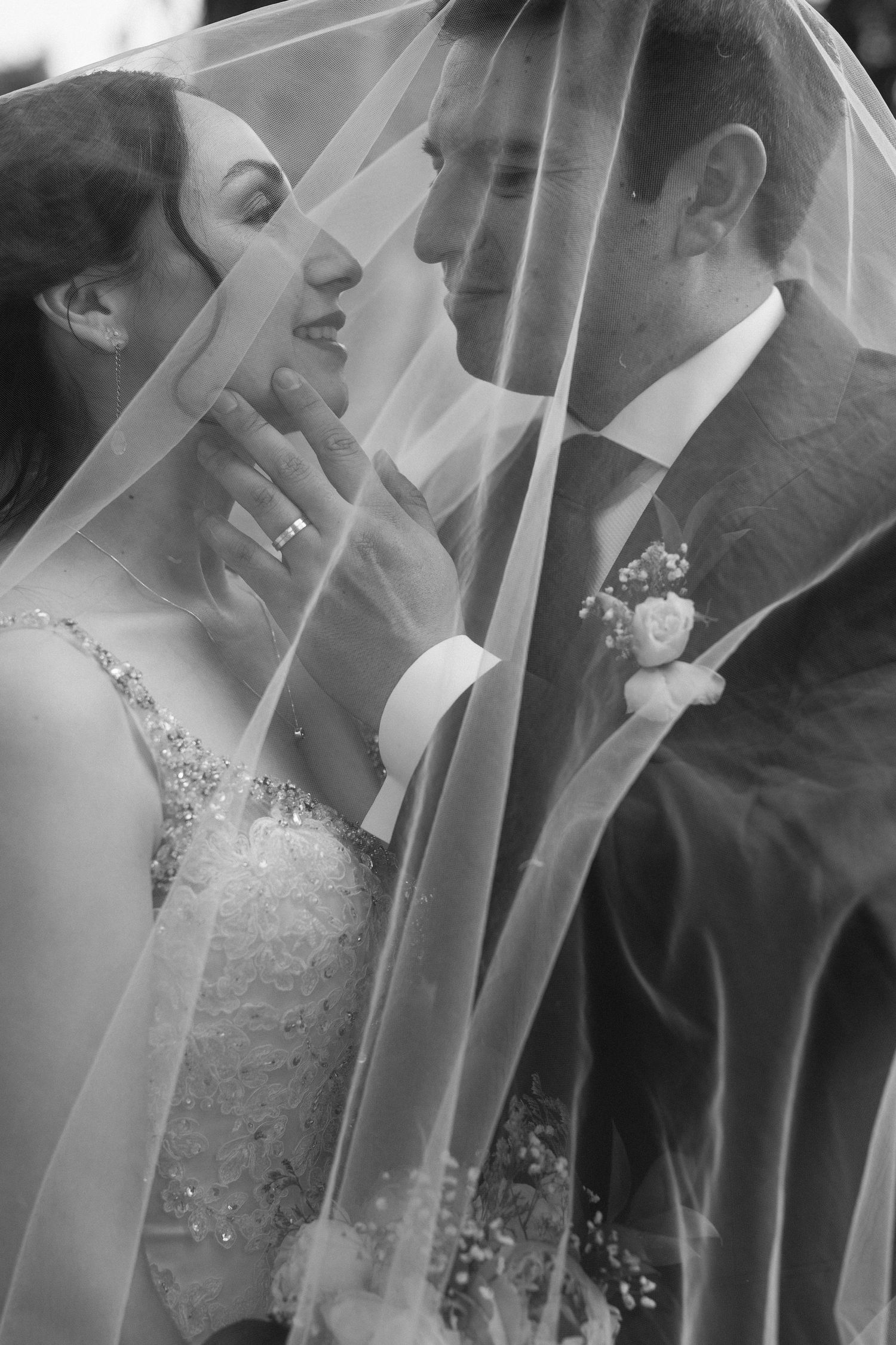 Romantic black and white portrait of newlyweds under a flowing veil.