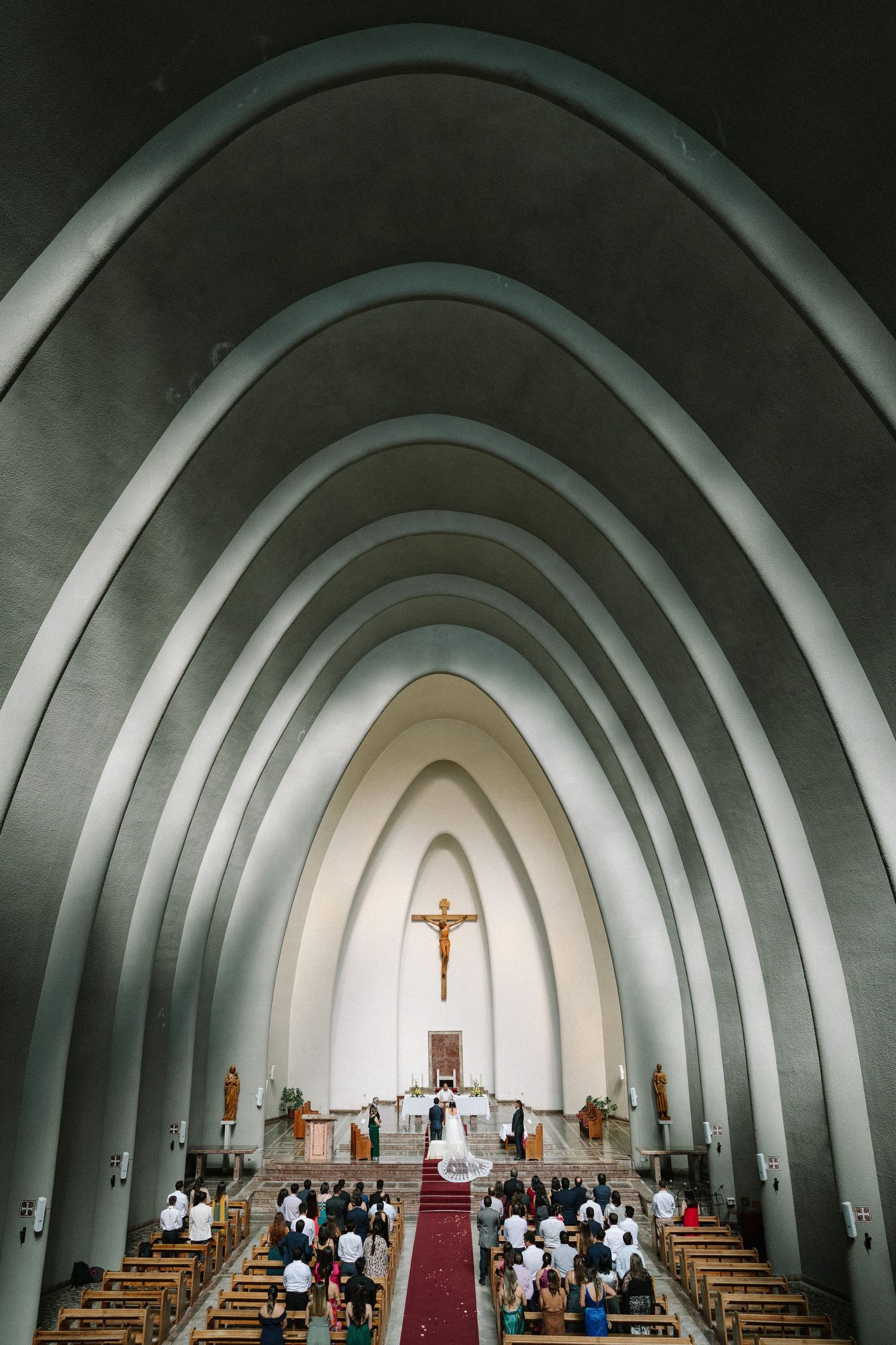 An architectural view of a church interior with dramatic arched ceiling and crucifix.