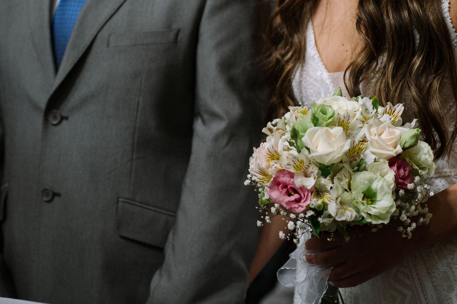 A close-up of a bridal bouquet with roses next to a gray suit.