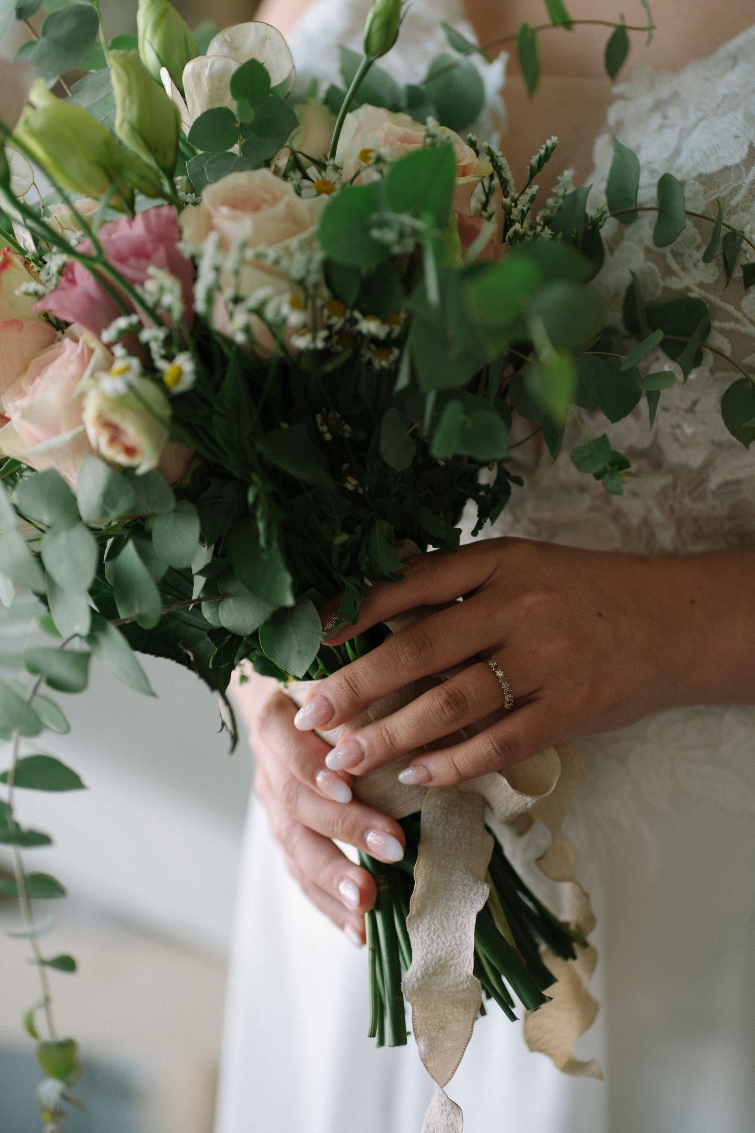 Elegant bridal bouquet with pink roses and eucalyptus held by hands with wedding ring.