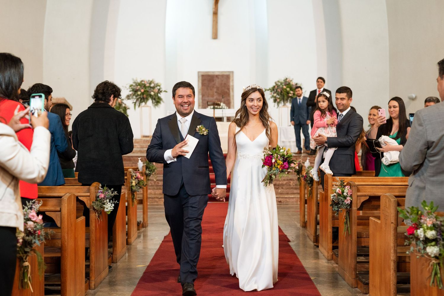 Happy newlyweds walk down church aisle after ceremony while guests celebrate.