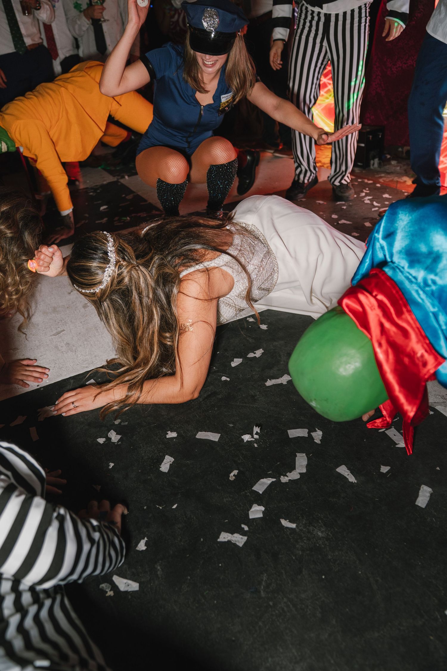 Wedding party guests lying on dance floor with balloons and confetti during celebration.