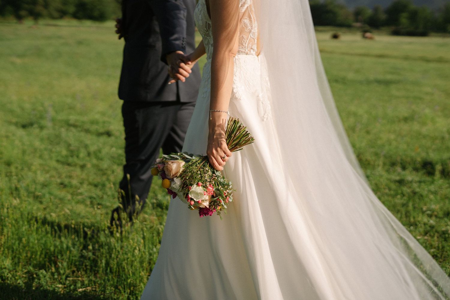 A side view of a wedding dress and bouquet against a green meadow background.