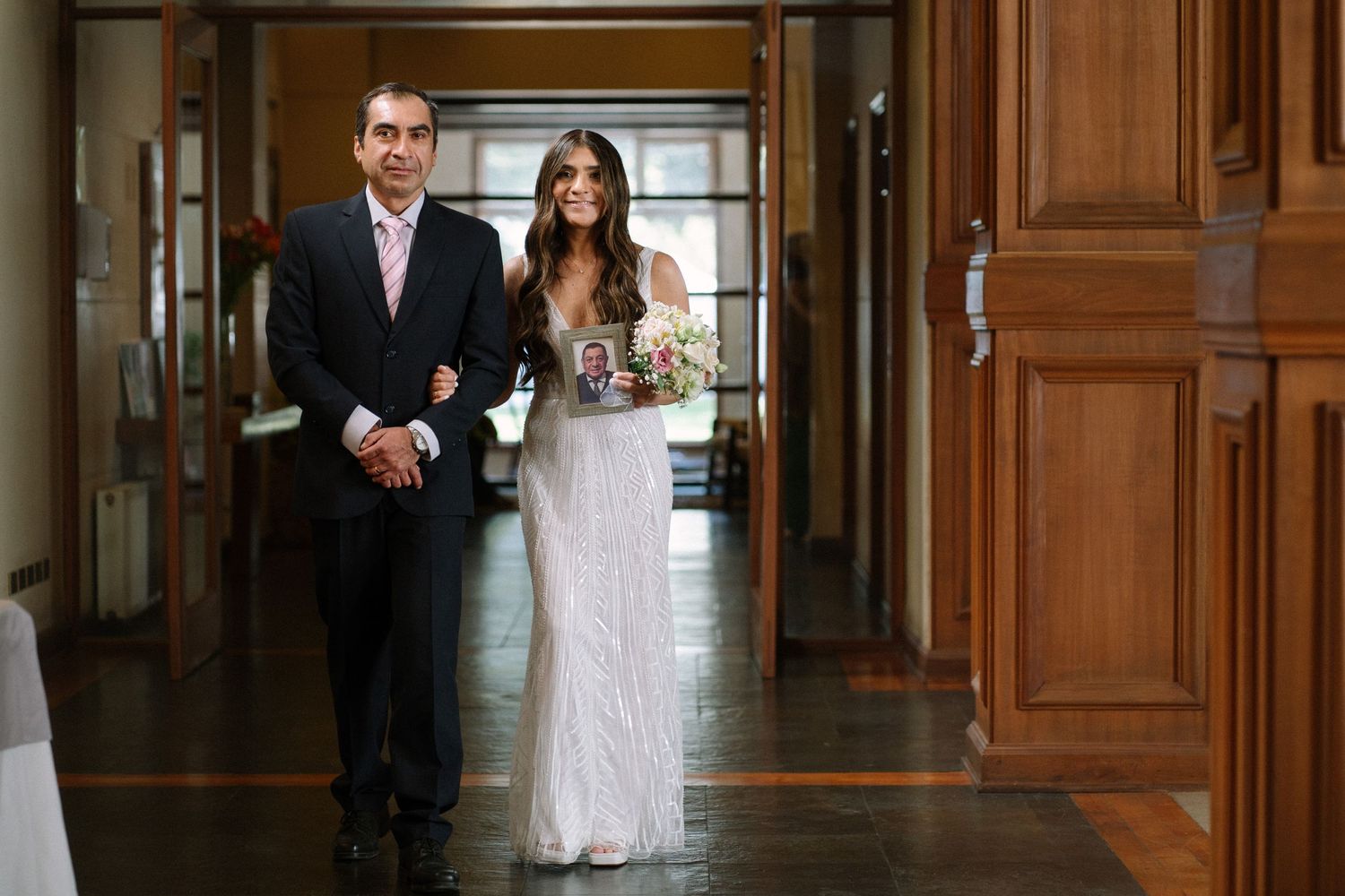 A couple walking through an elegant hallway with wood paneling and natural light.