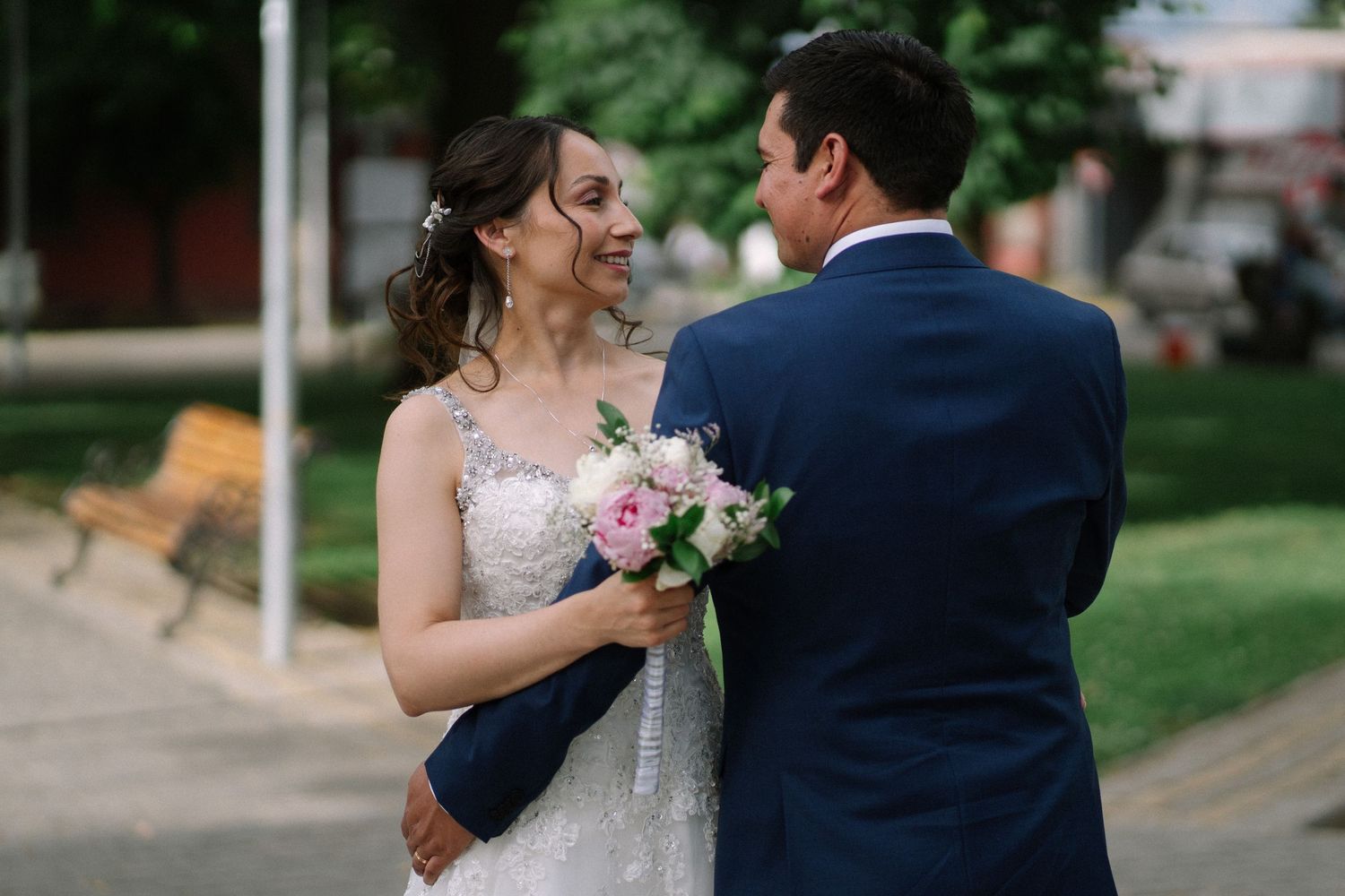 Couple shares intimate moment outdoors with bride holding pink bouquet.