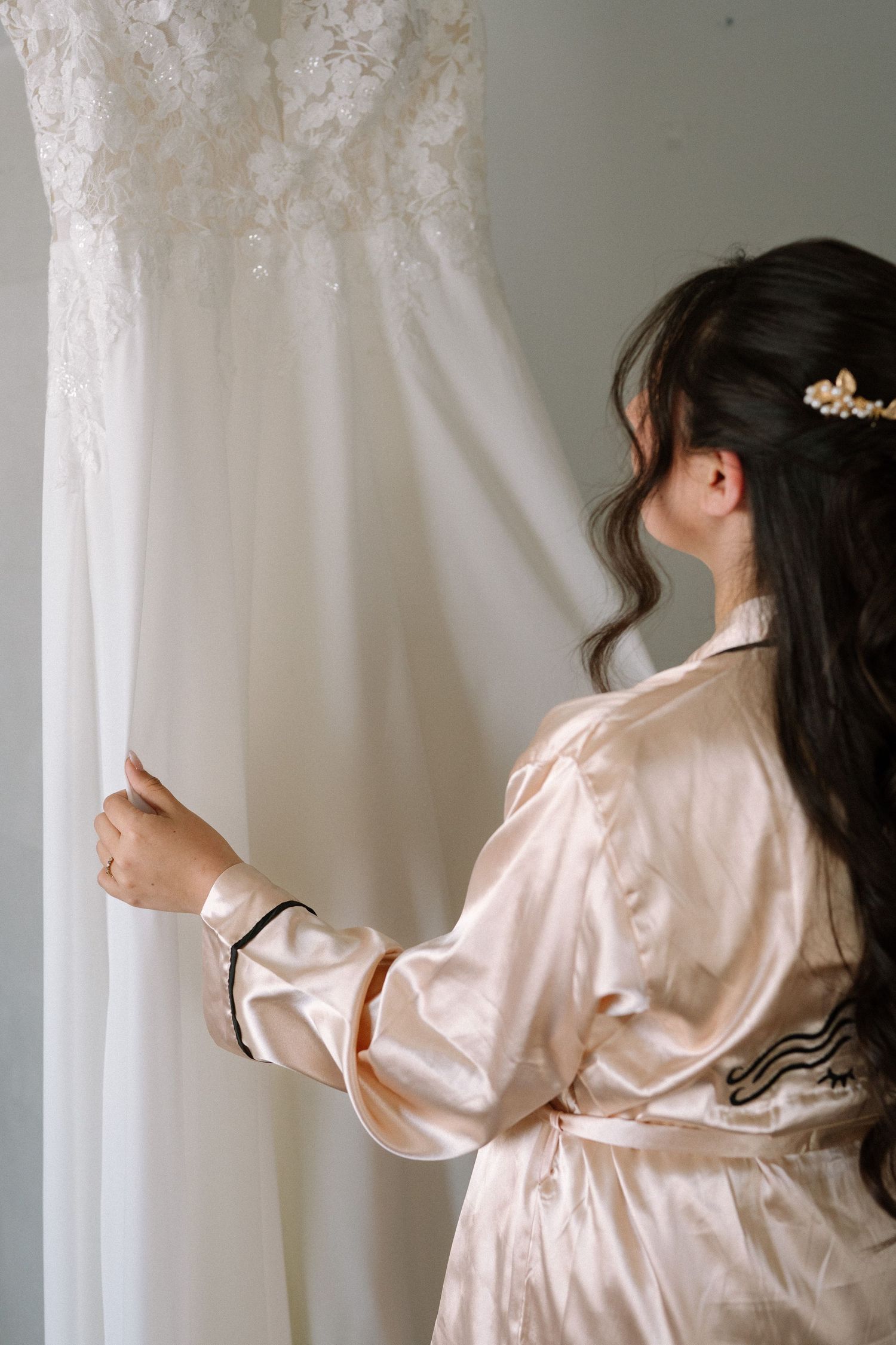 Side view of person in silk robe examining white wedding gown details.