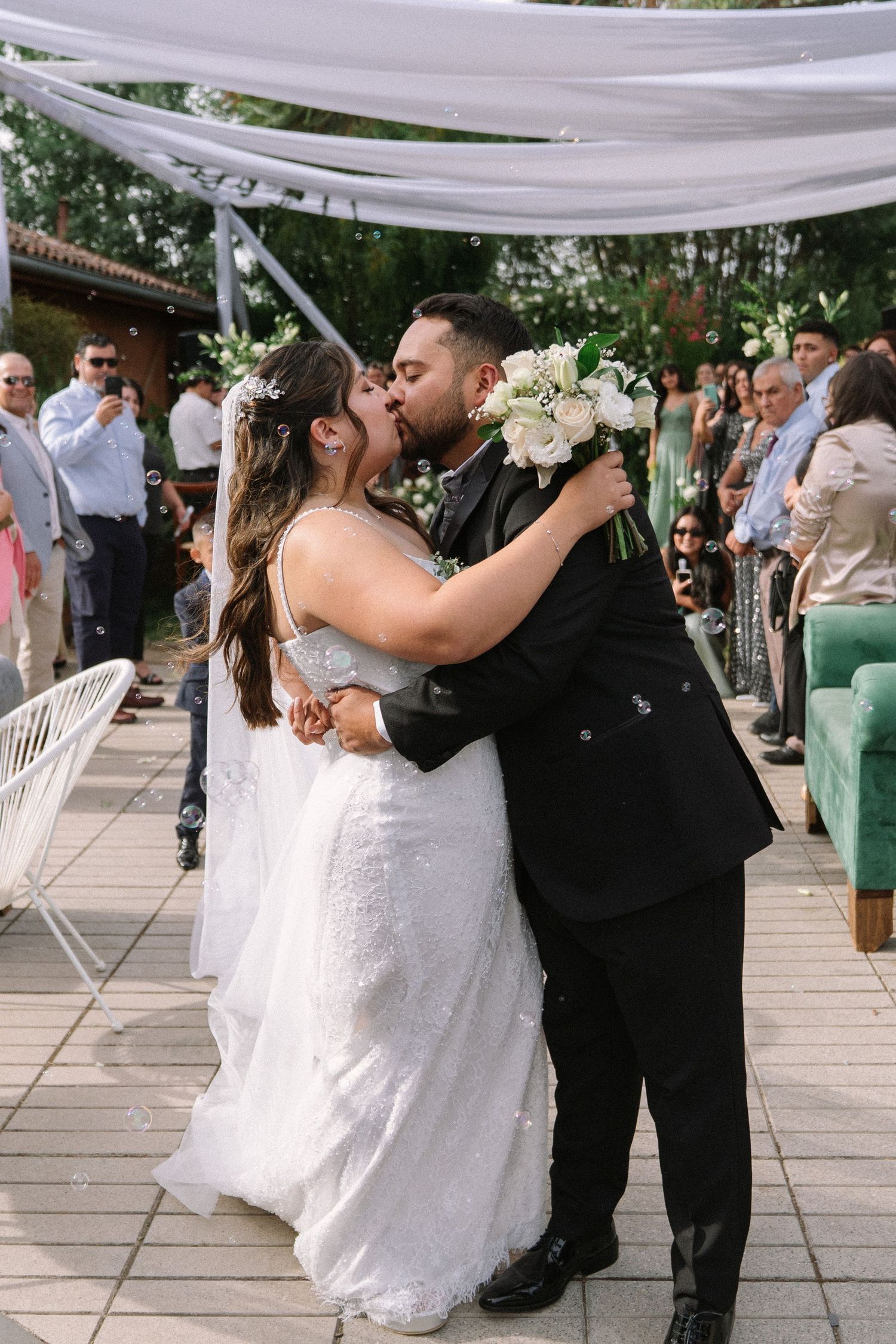 Bride and groom share a romantic kiss at the altar during their outdoor wedding ceremony with guests looking on.