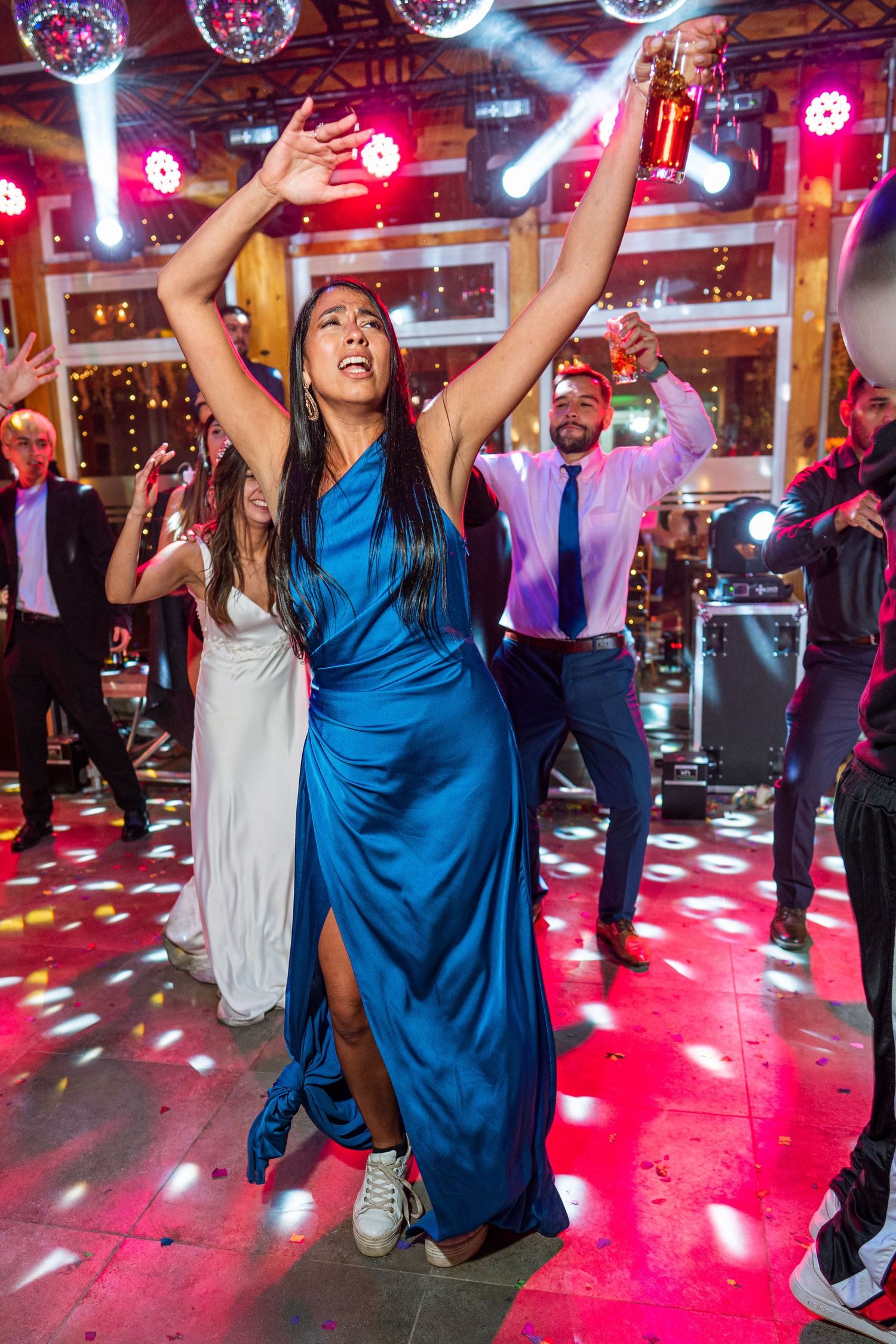 Person in blue gown dances enthusiastically under disco balls with arms raised at a party.