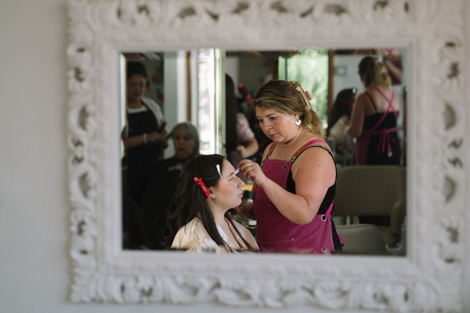 Reflection in ornate white mirror shows makeup application in progress.