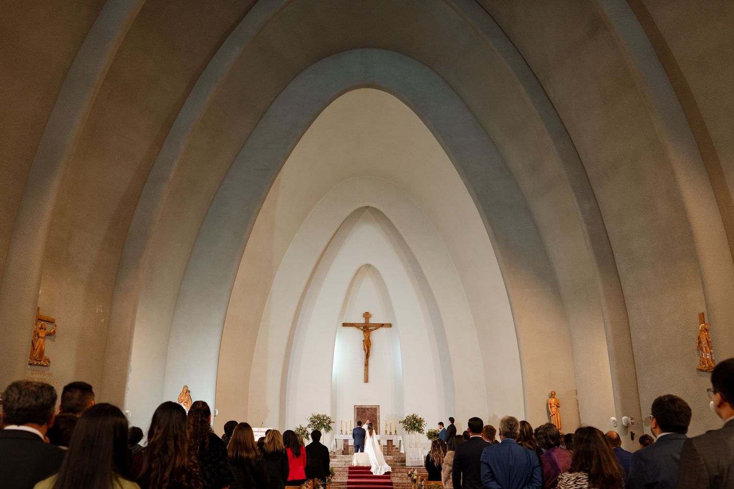 Wedding ceremony in a modern church with dramatic arched architecture and gathered congregation.