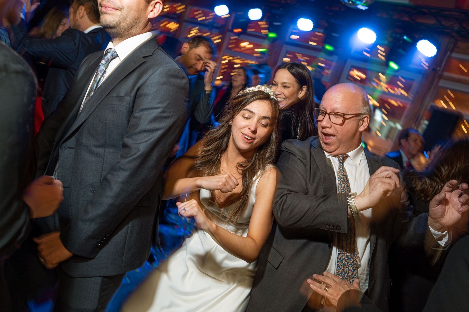 Wedding guests dancing energetically under blue party lights at a reception celebration.