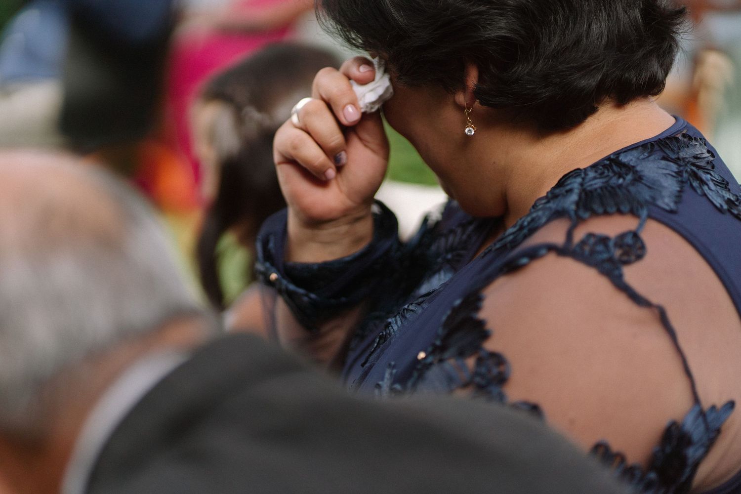 Emotional wedding guest wiping tears with a tissue during an outdoor wedding ceremony.