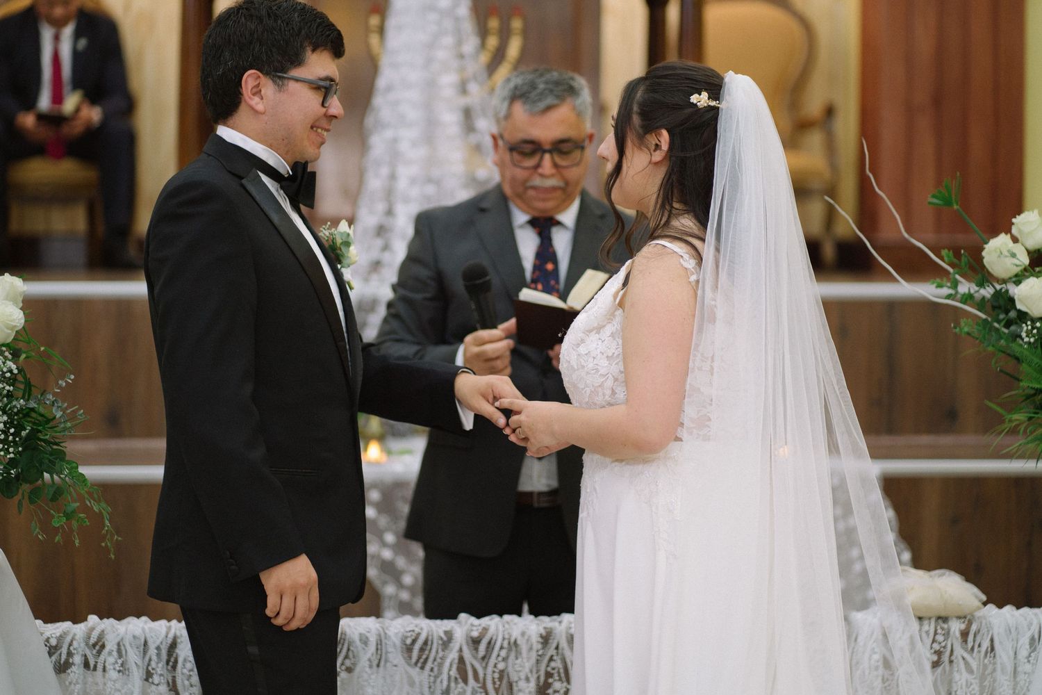A wedding ceremony takes place in a church with an officiant performing the service at the altar.
