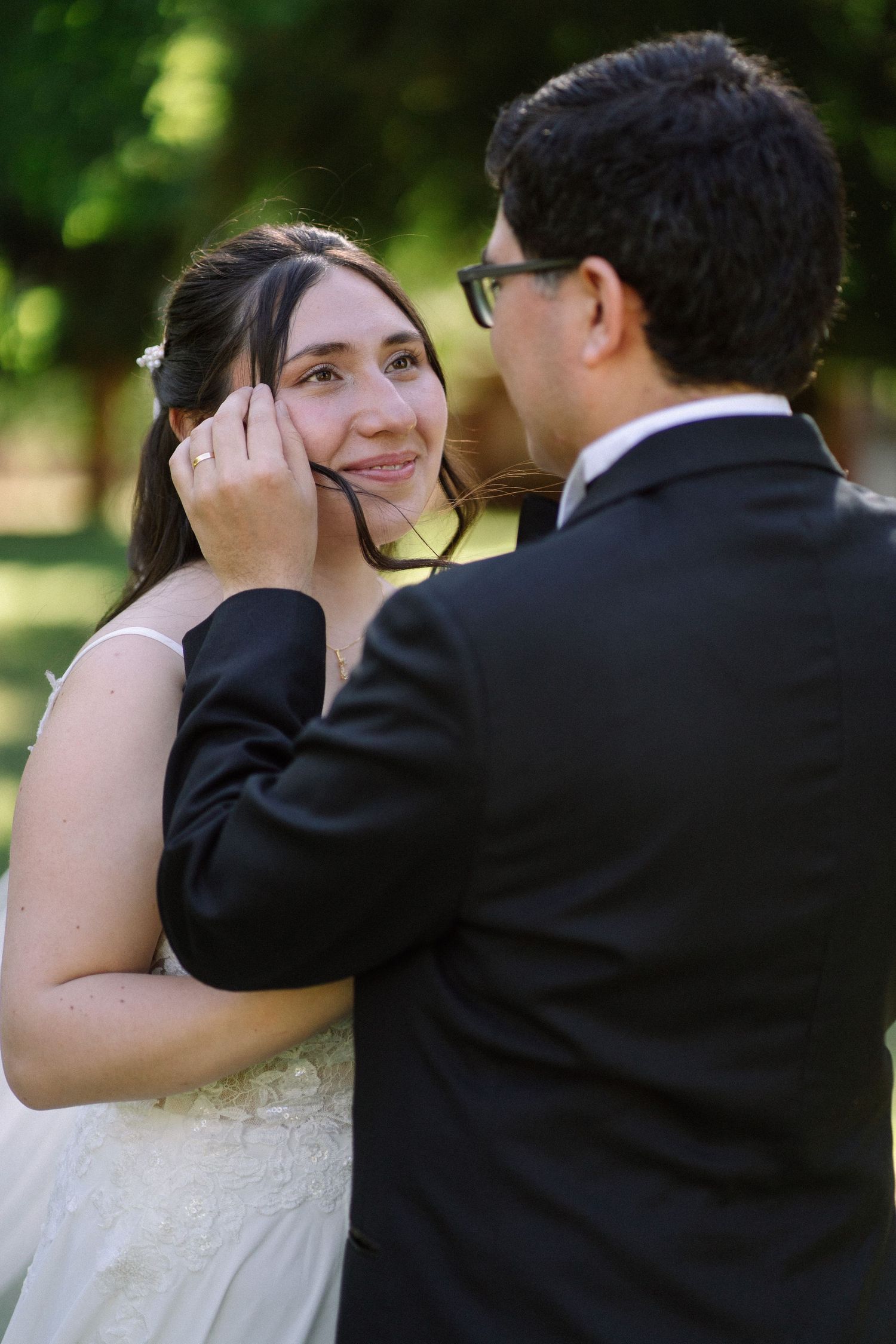 An intimate wedding moment captured during a gentle caress in a sunlit outdoor setting.