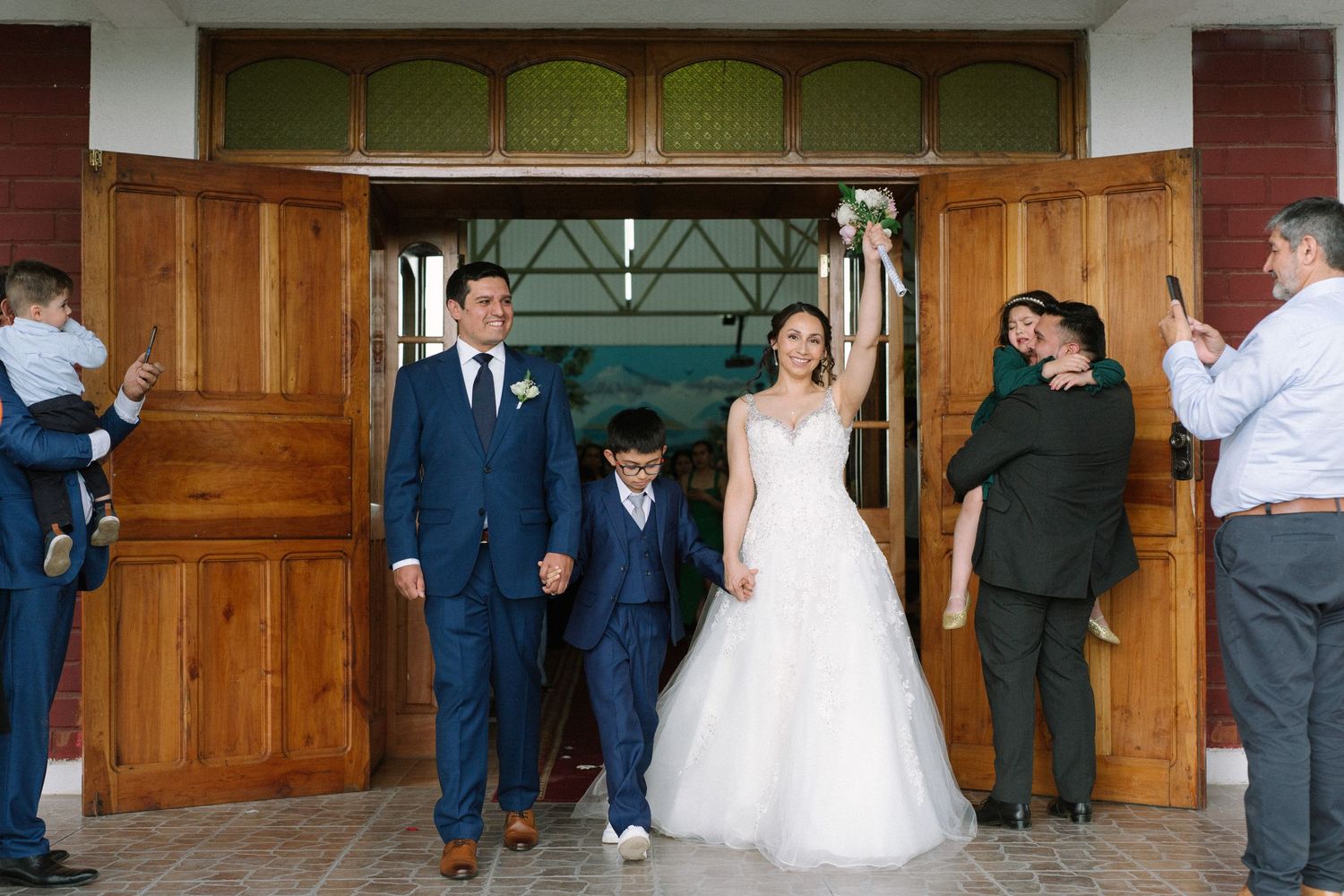 Wedding party exits wooden church doors after ceremony.