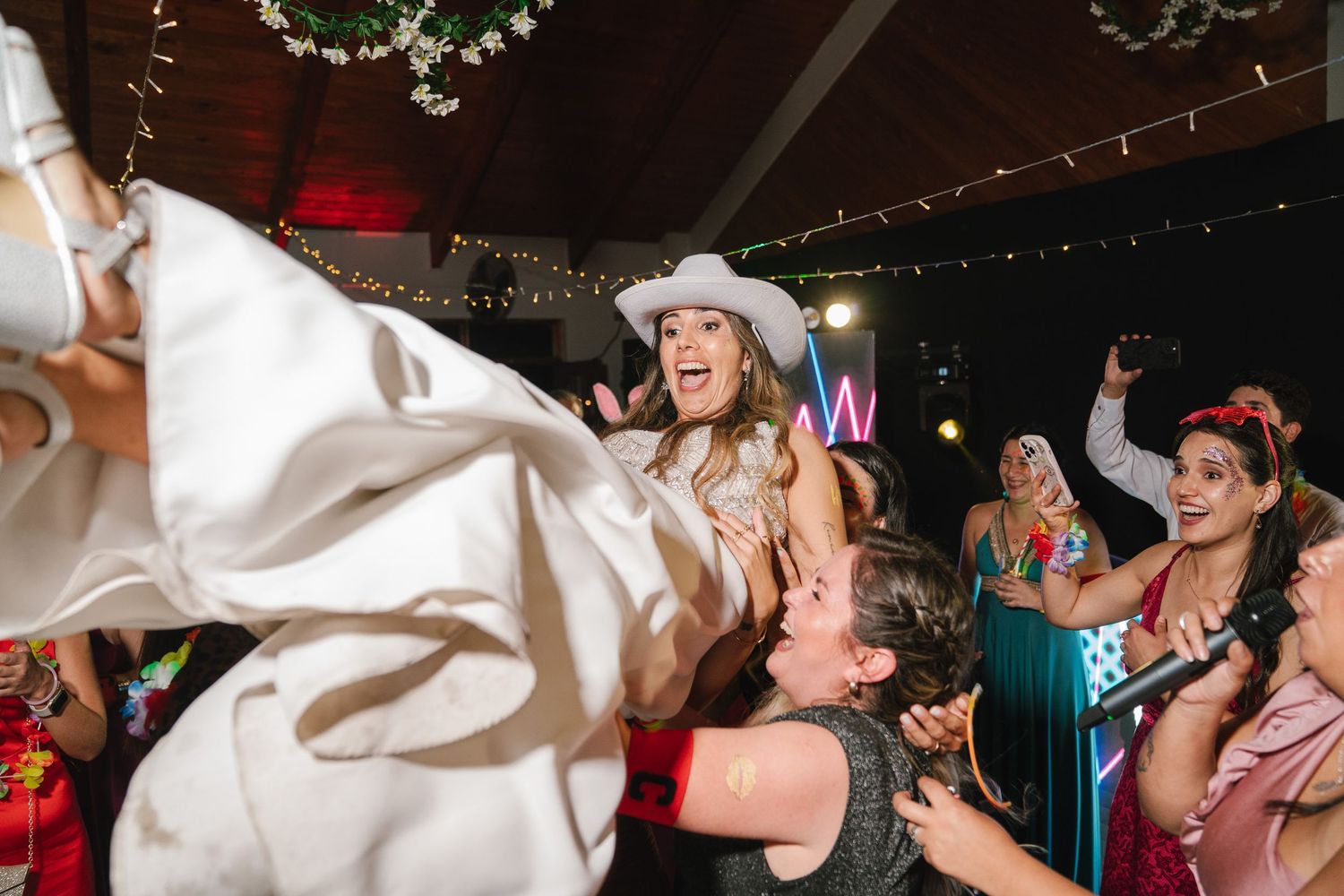 Wedding guests dance and celebrate while a white veil flows through the air during a reception party.