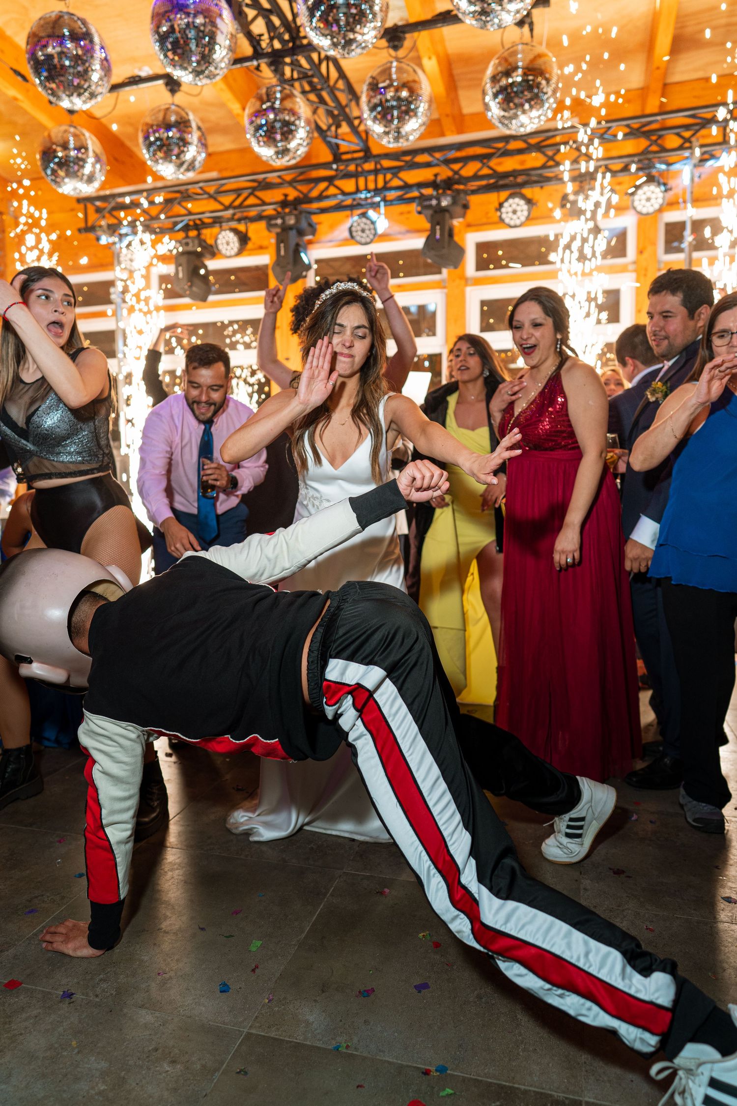 Dancers perform energetic moves at a party under disco lights and sparklers.