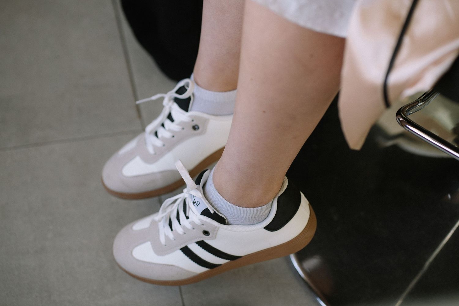 A person wearing white Adidas sneakers with black stripes and white socks.