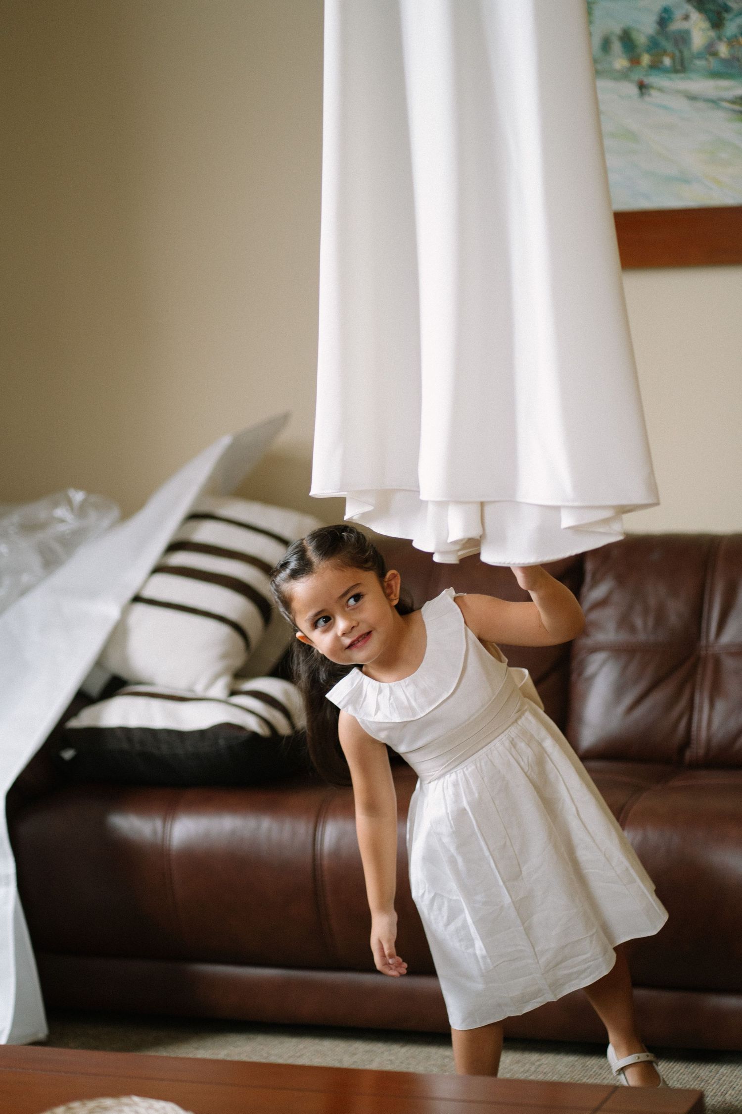 A sequence of four photos showing someone in a white dress playfully posing on a brown leather couch.