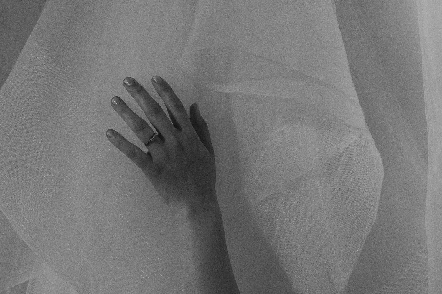 Hand reaching through delicate white wedding veil fabric creating artistic silhouette.