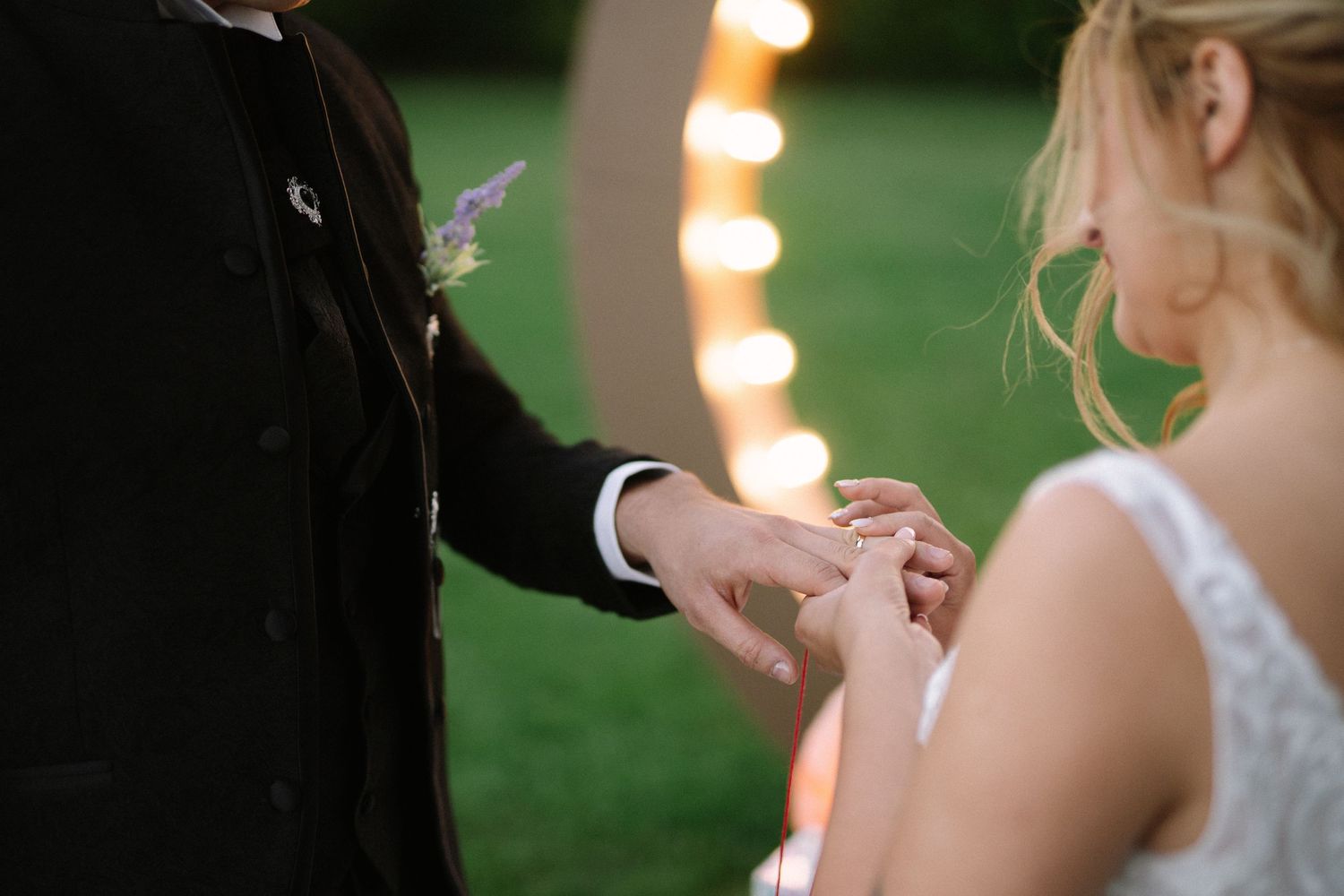 Close-up shot of wedding ring exchange between bride and groom during outdoor ceremony.