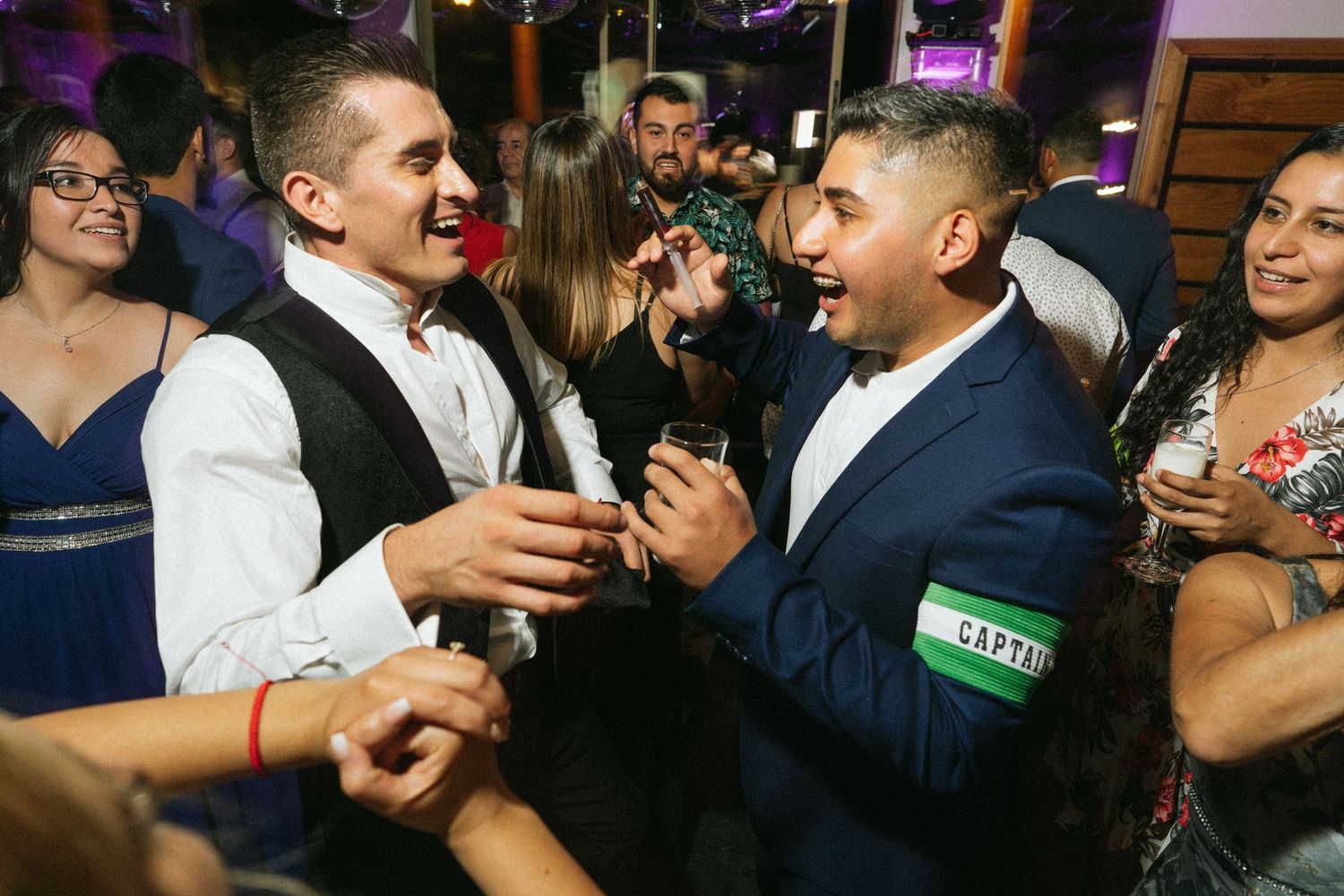 Party guests laughing and celebrating at a nighttime event with purple lighting.
