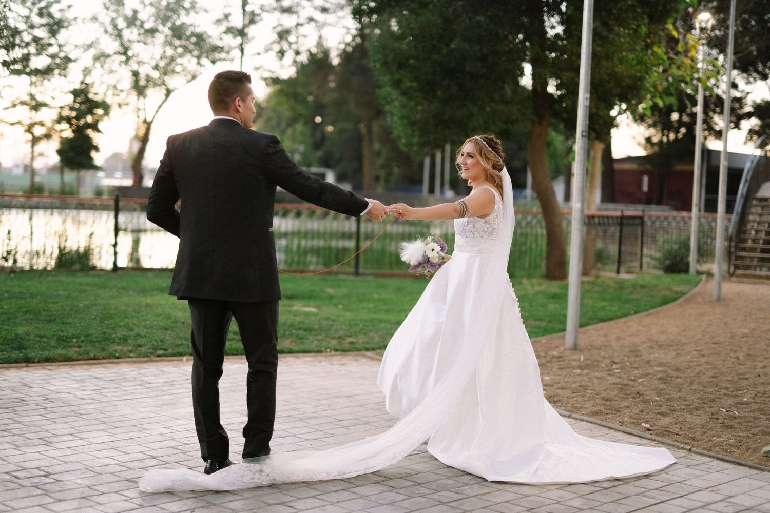 Newlyweds hold hands while dancing on a paved path during their wedding photoshoot.
