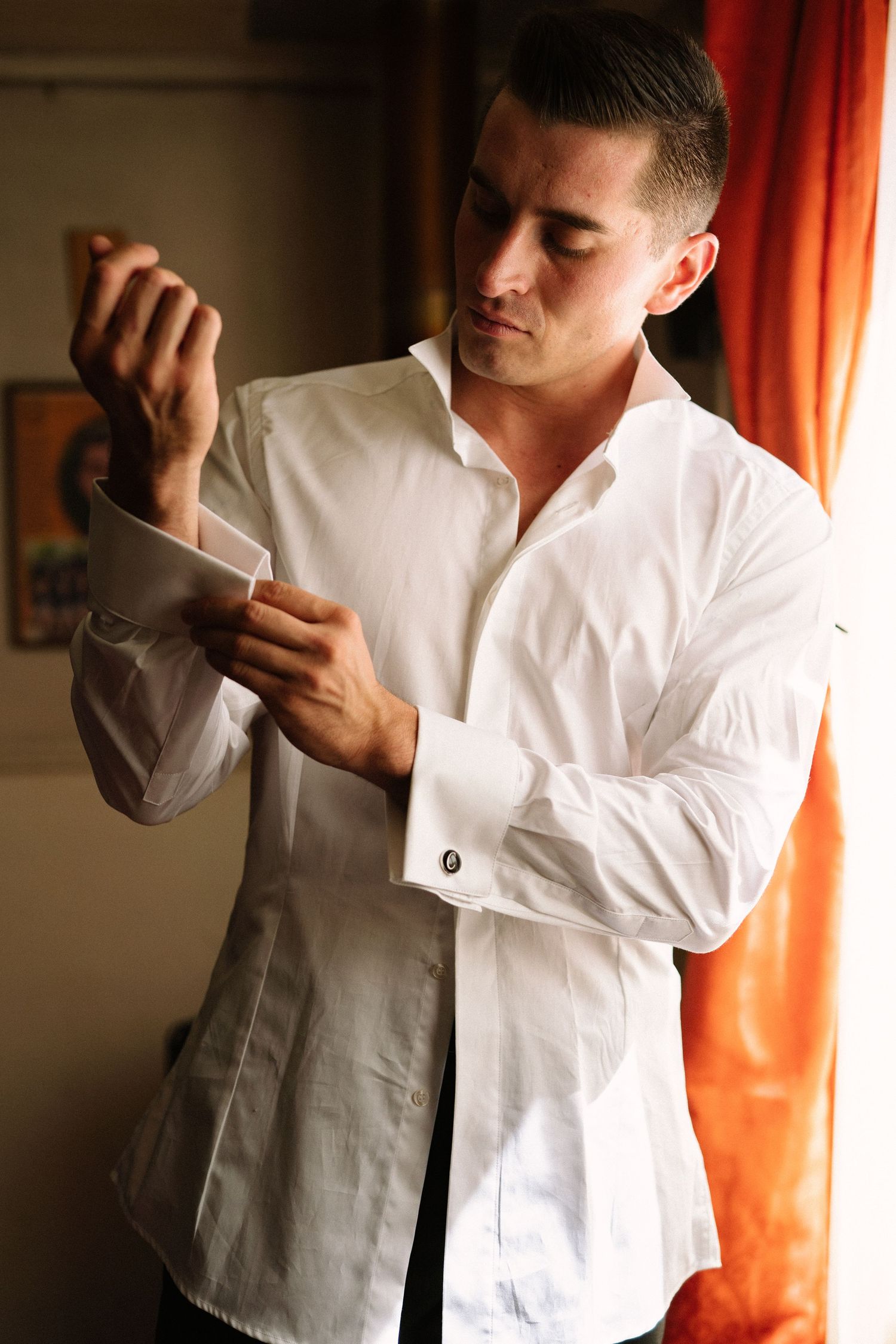 Person in white dress shirt adjusting their sleeve in front of orange curtains.