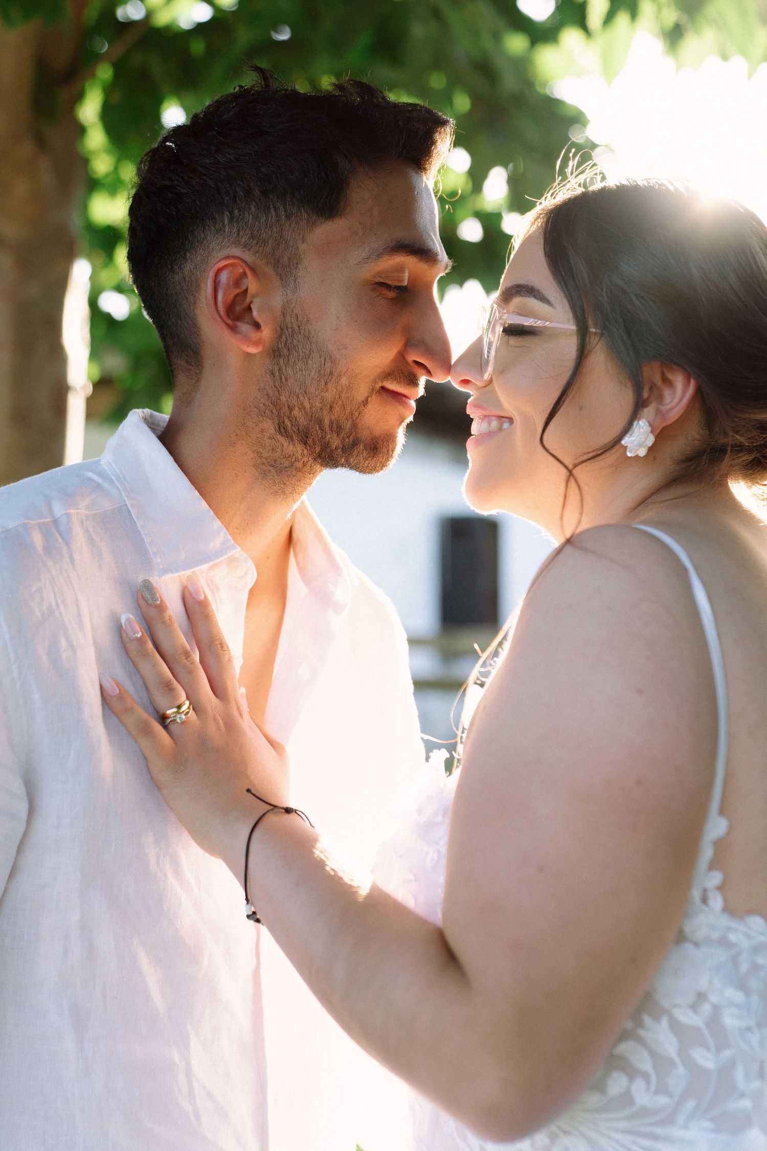 Bride and groom lean in for a kiss bathed in golden sunlight outdoors.